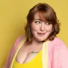 A red-haired woman in a pink cardigan against a yellow background.